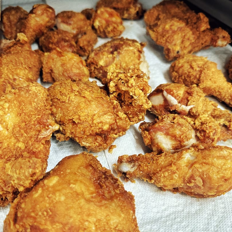 Golden brown fried chicken pieces, including drumsticks and thighs, resting on a white paper towel.